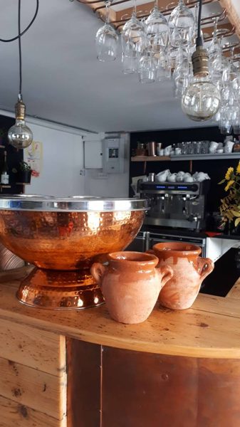 A bar with a copper ice bucket, pots and hanging glasses.