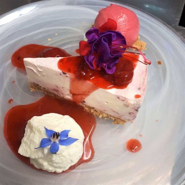 A berry dessert on a white plate with an edible flower and a quenelle of cream.
