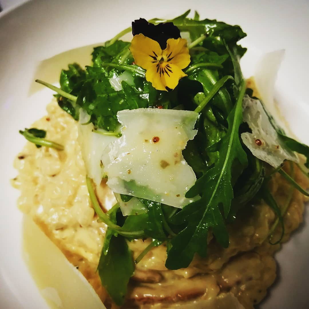 A creamy dish topped with shaved cheese, rocket and a pansy.