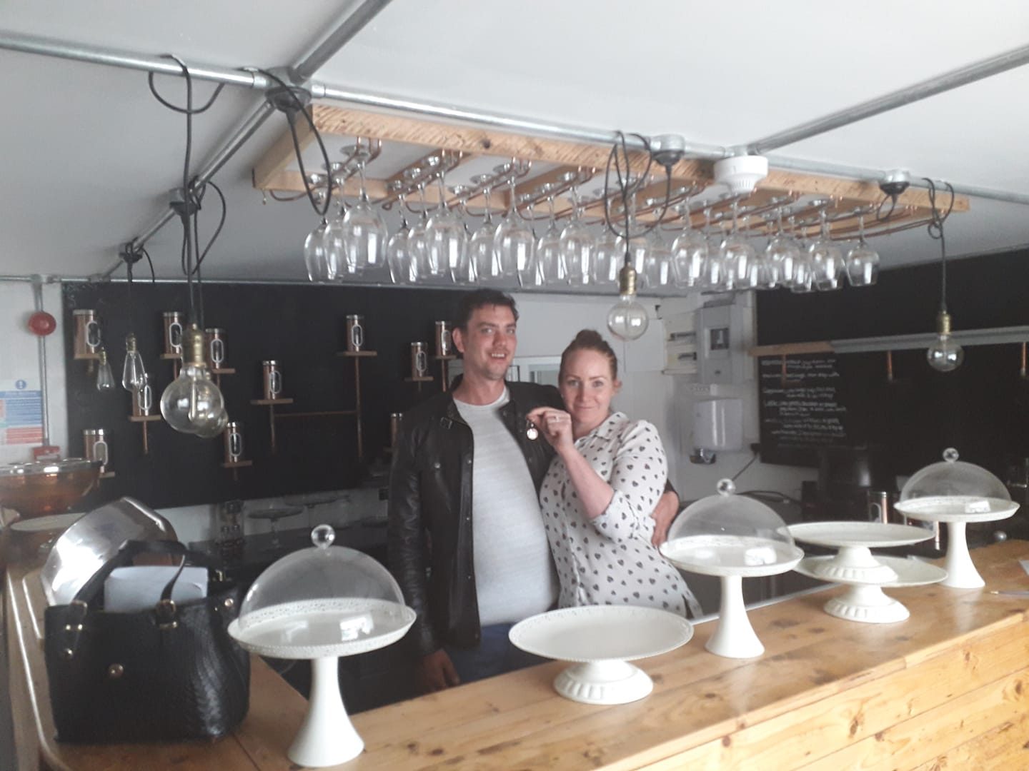 A man and a woman smiling behind the bar, with cake stands in front of them.