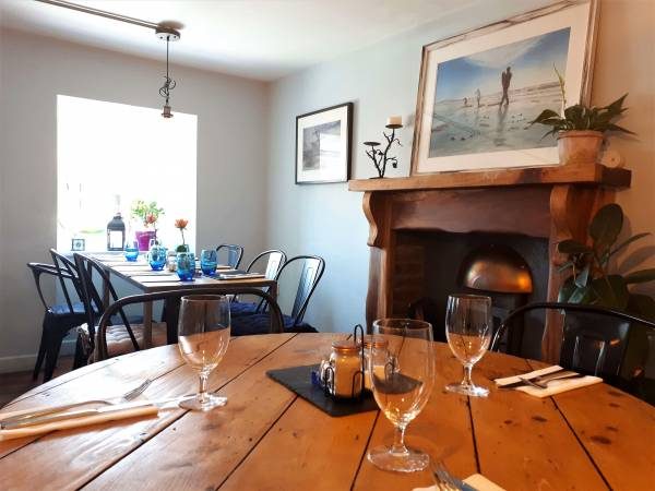 A dining room with a fireplace, framed pictures and a wooden table set with glasses.