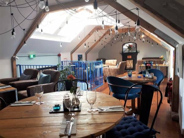 A dining room with a sloping timber ceiling, skylights and set tables.